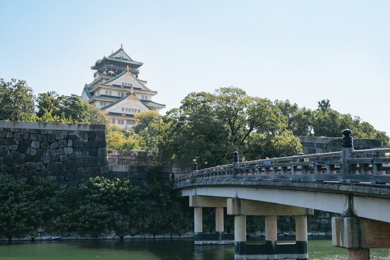 Osaka Castle with a traditional wooden bridge on a sunny day - visitor approach
