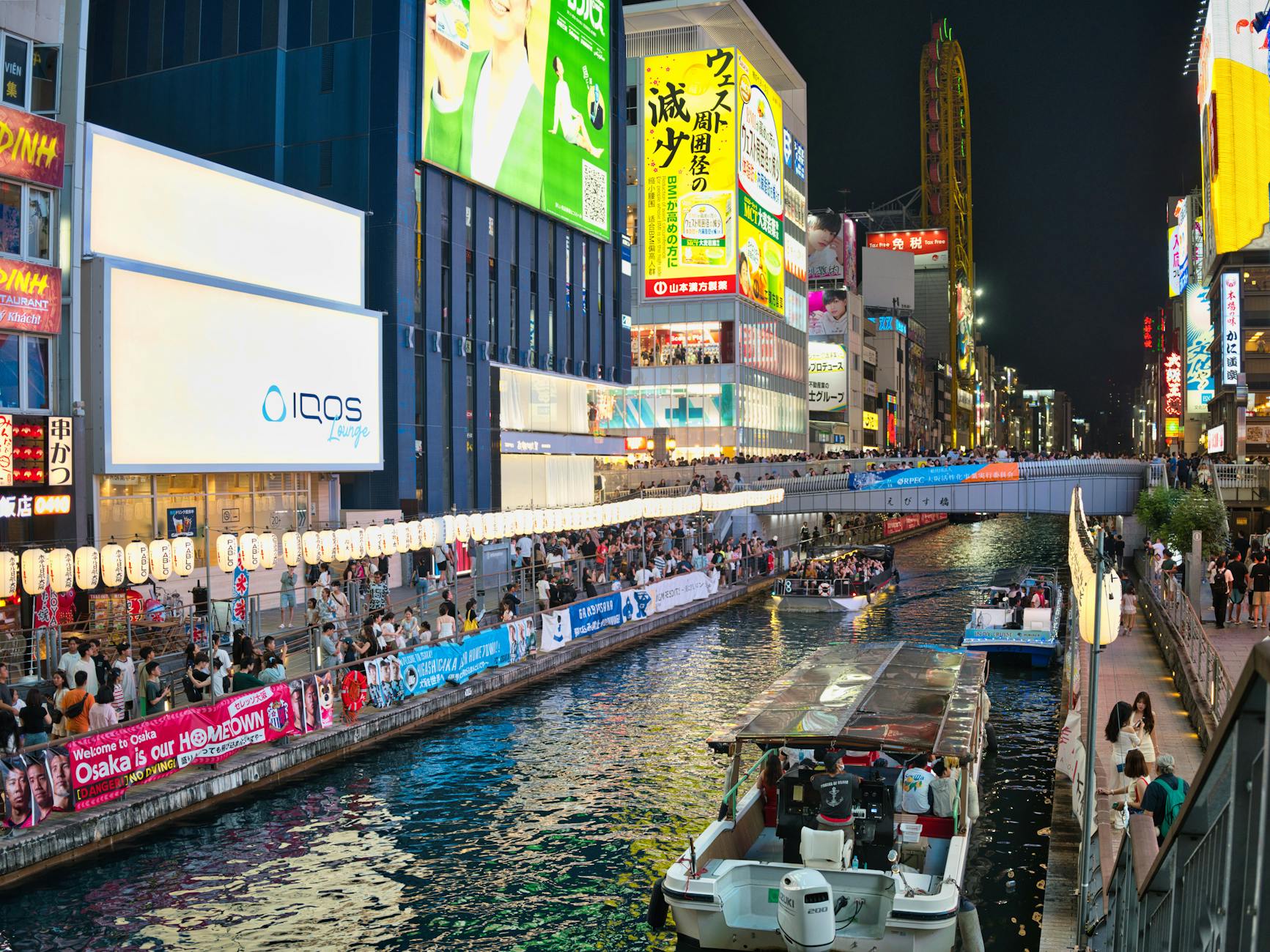 Osaka river cruise boat passing under illuminated bridges at night