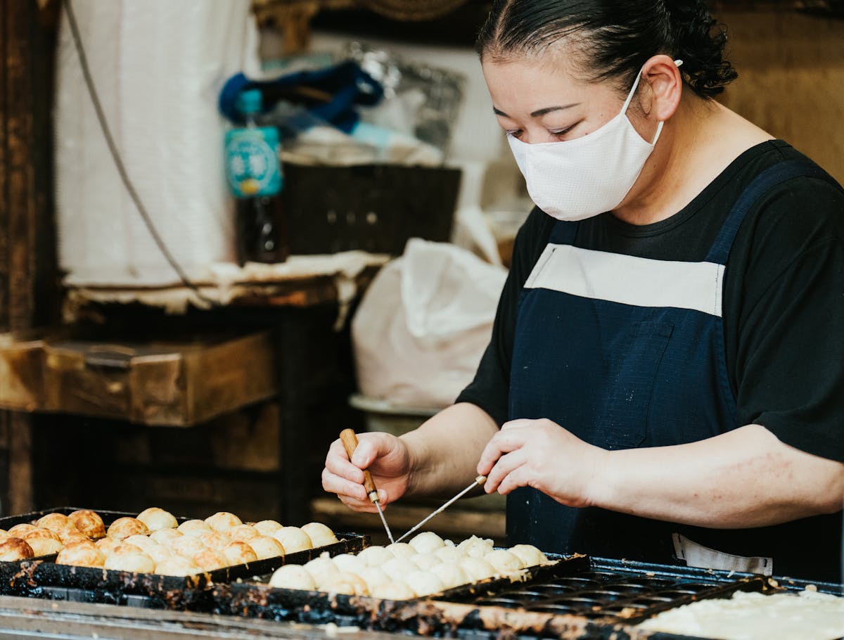 Street food vendor preparing fresh golden takoyaki octopus balls at an outdoor market in Osaka