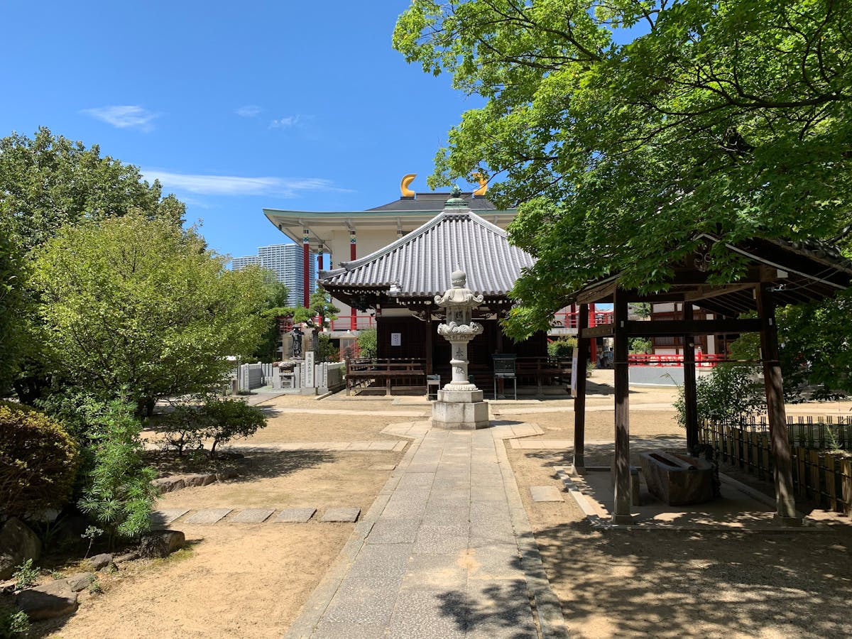 Traditional Japanese temple in Osaka surrounded by lush green trees under a blue sky