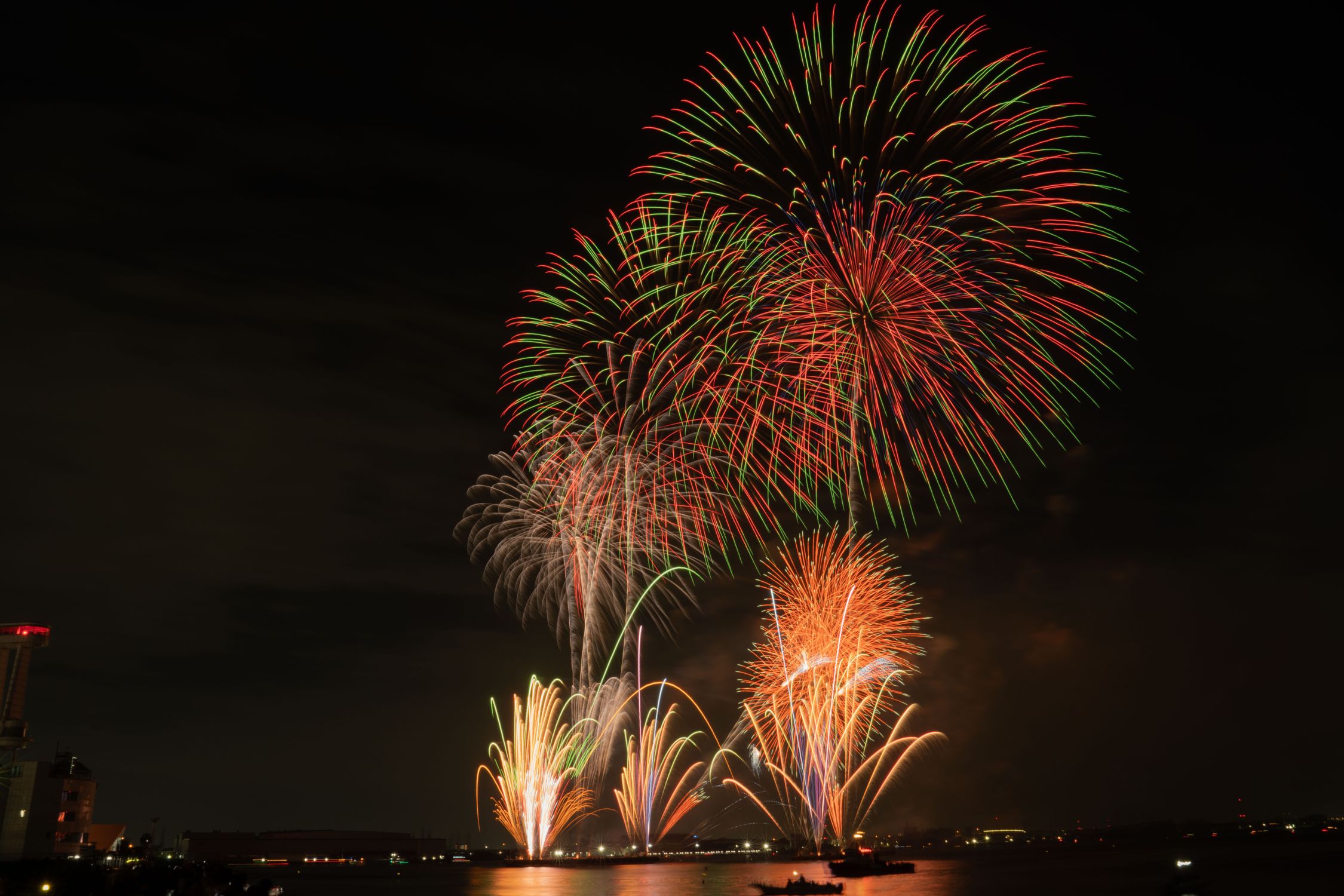 Summer fireworks bursting over water at night, like the Osaka festivals fireworks finales