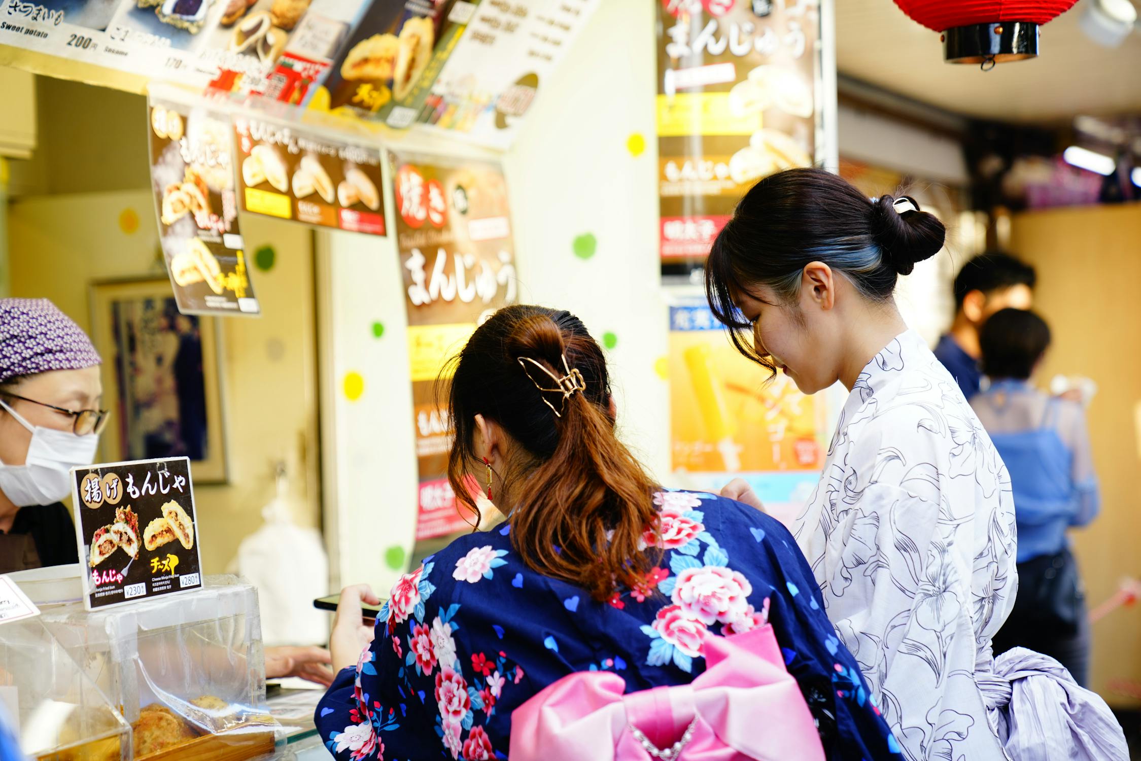 Women in yukata ordering at a Japanese street food stall during a summer festival in Osaka