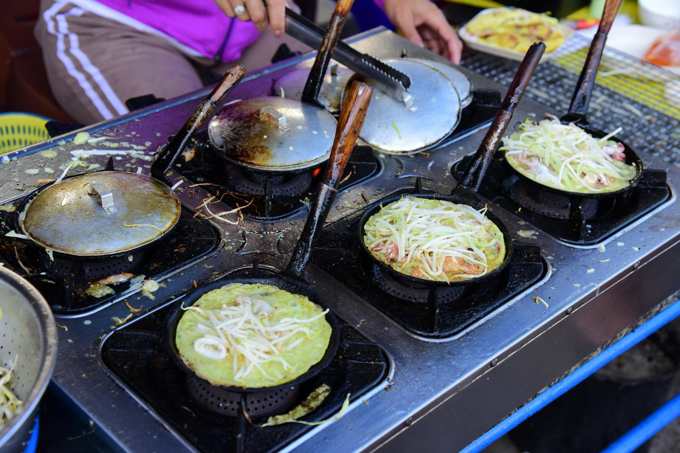 A cook making a savory okonomiyaki pancake on a hot teppan griddle in Osaka