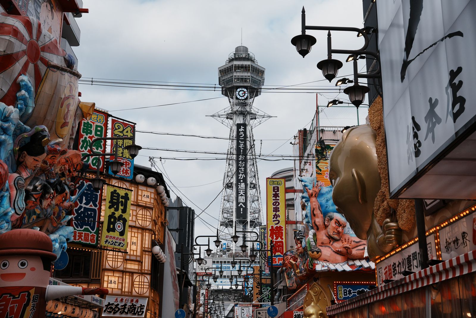 A retro street in Shinsekai with shop signs leading toward Tsutenkaku Tower, Osaka
