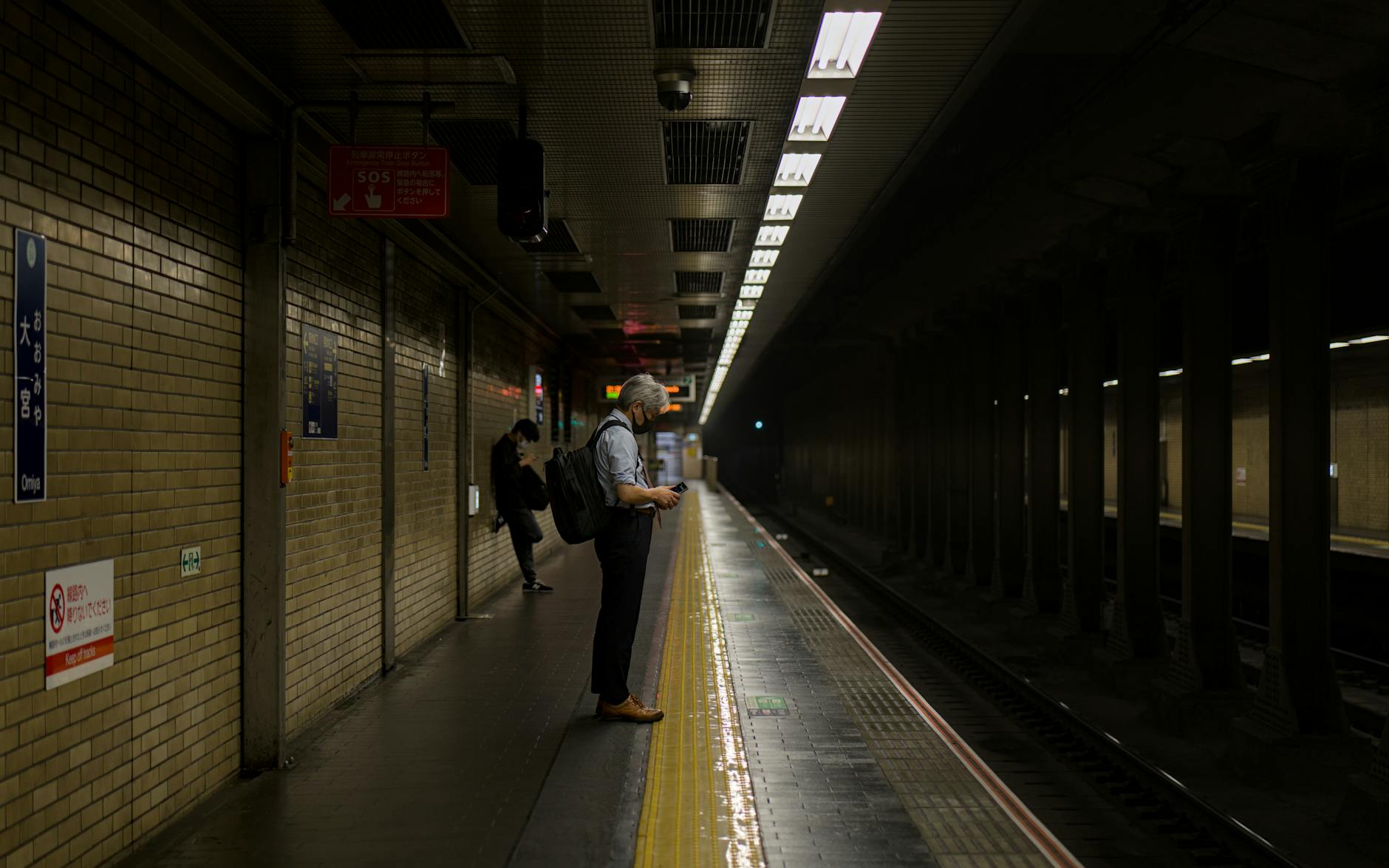 A man waits alone on a quiet subway platform at night in Japan where mobile signal can drop
