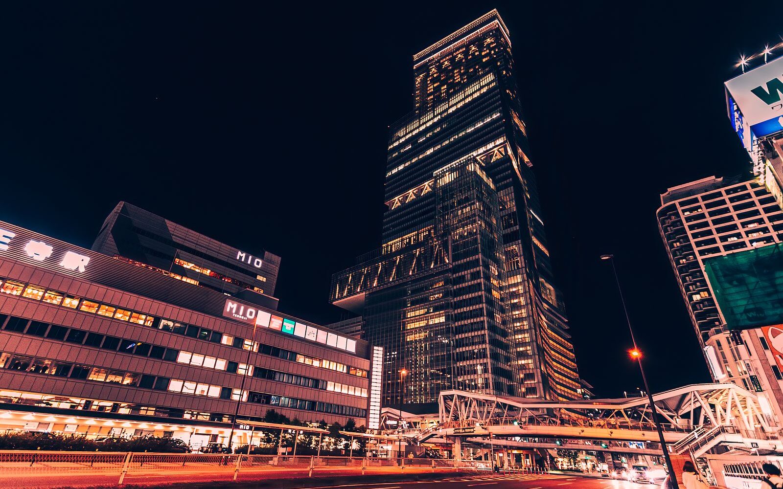 Abeno Harukas lit up at night above the Tennoji Station forecourt, with the MIO building and the pedestrian footbridge in front