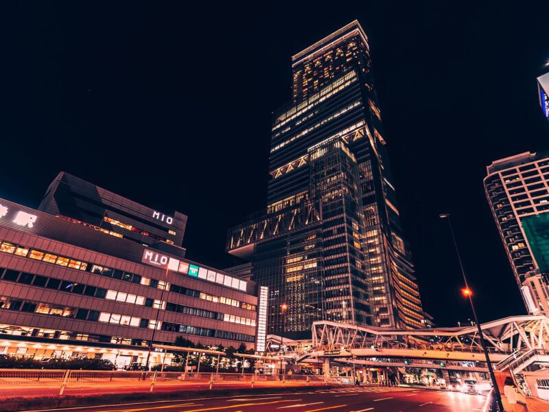 Abeno Harukas lit up at night above the Tennoji Station forecourt, with the MIO building and the pedestrian footbridge in front