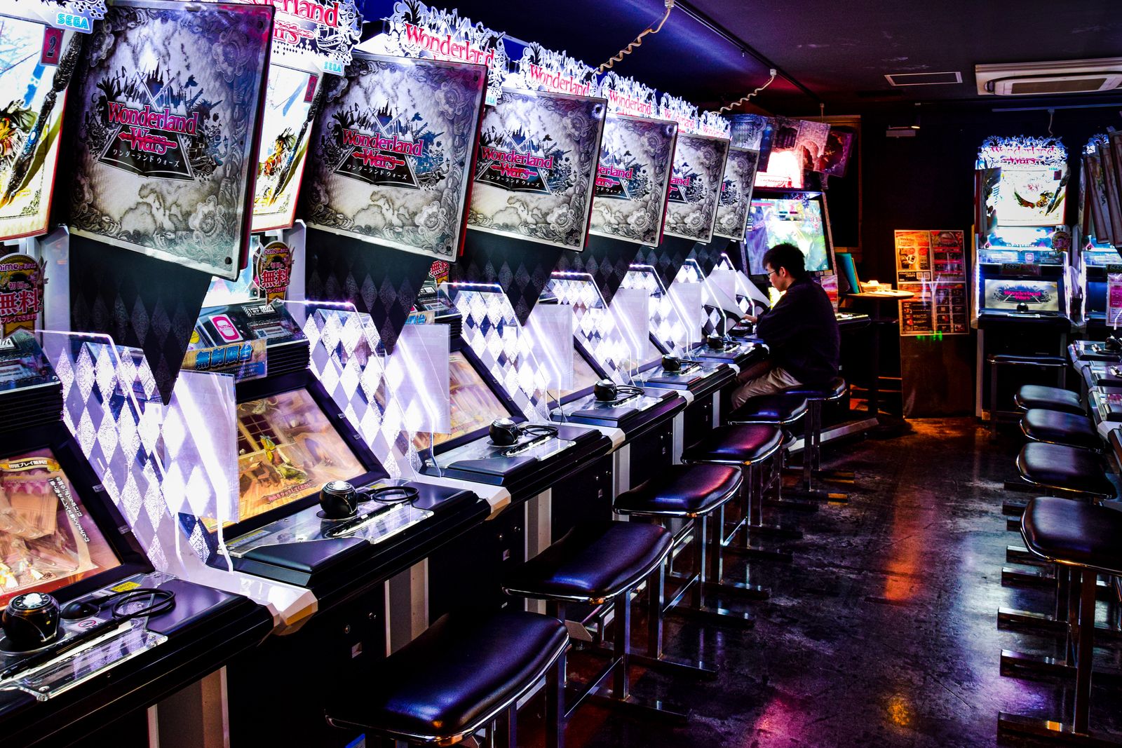 A long row of arcade cabinets with a lone player in a dim Japanese game centre