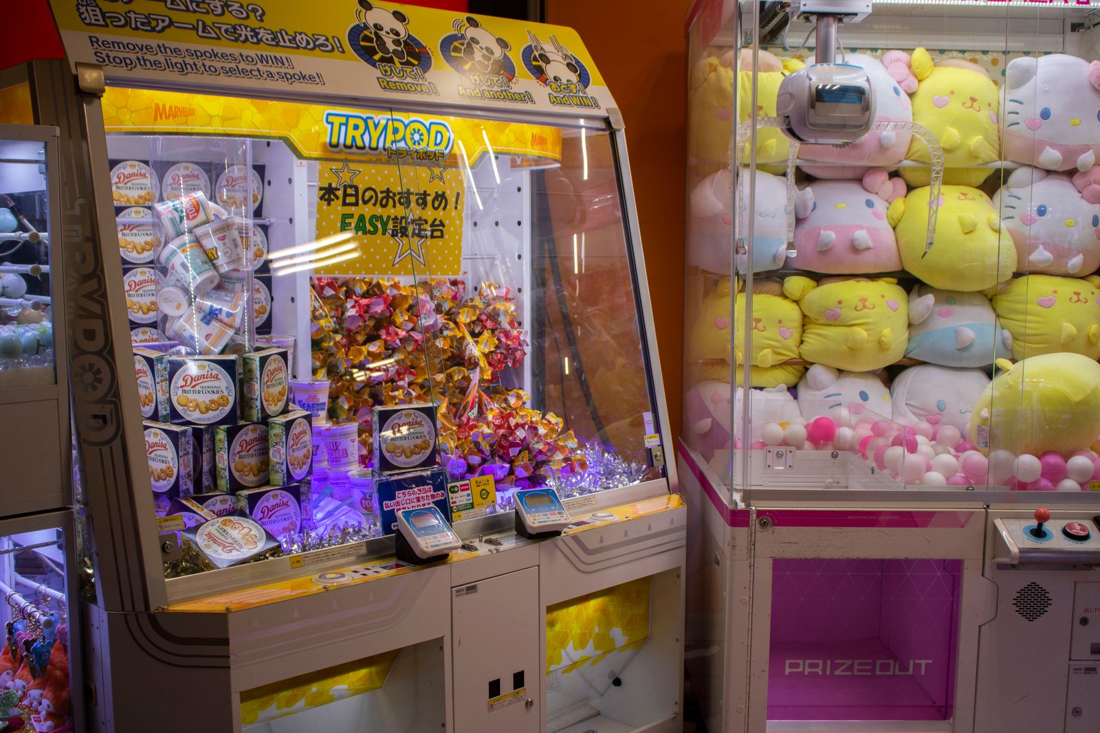 Crane games in a Japanese arcade, one filled with boxed snacks under a sign advertising an easy setting