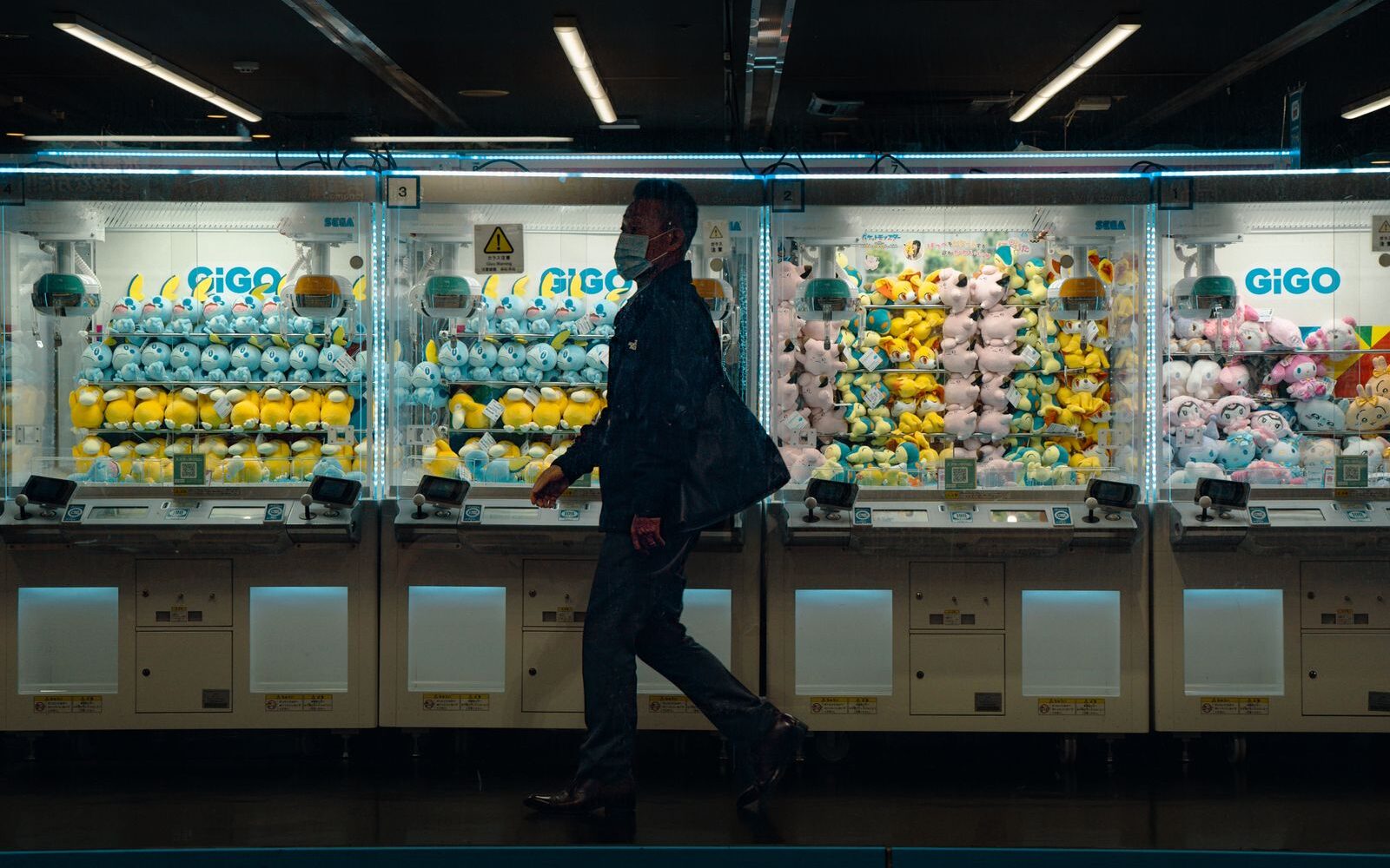 A man walking past a row of GiGO crane games stocked with plush toys