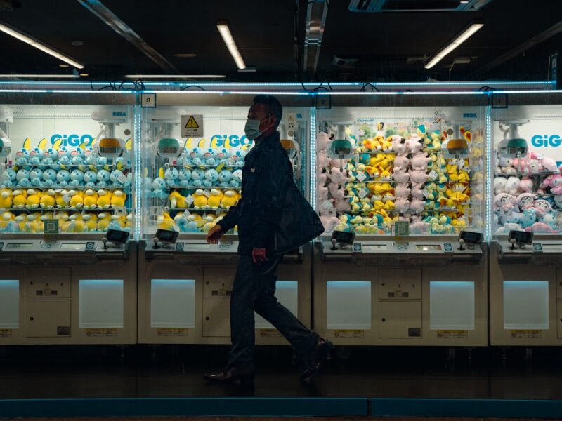 A man walking past a row of GiGO crane games stocked with plush toys