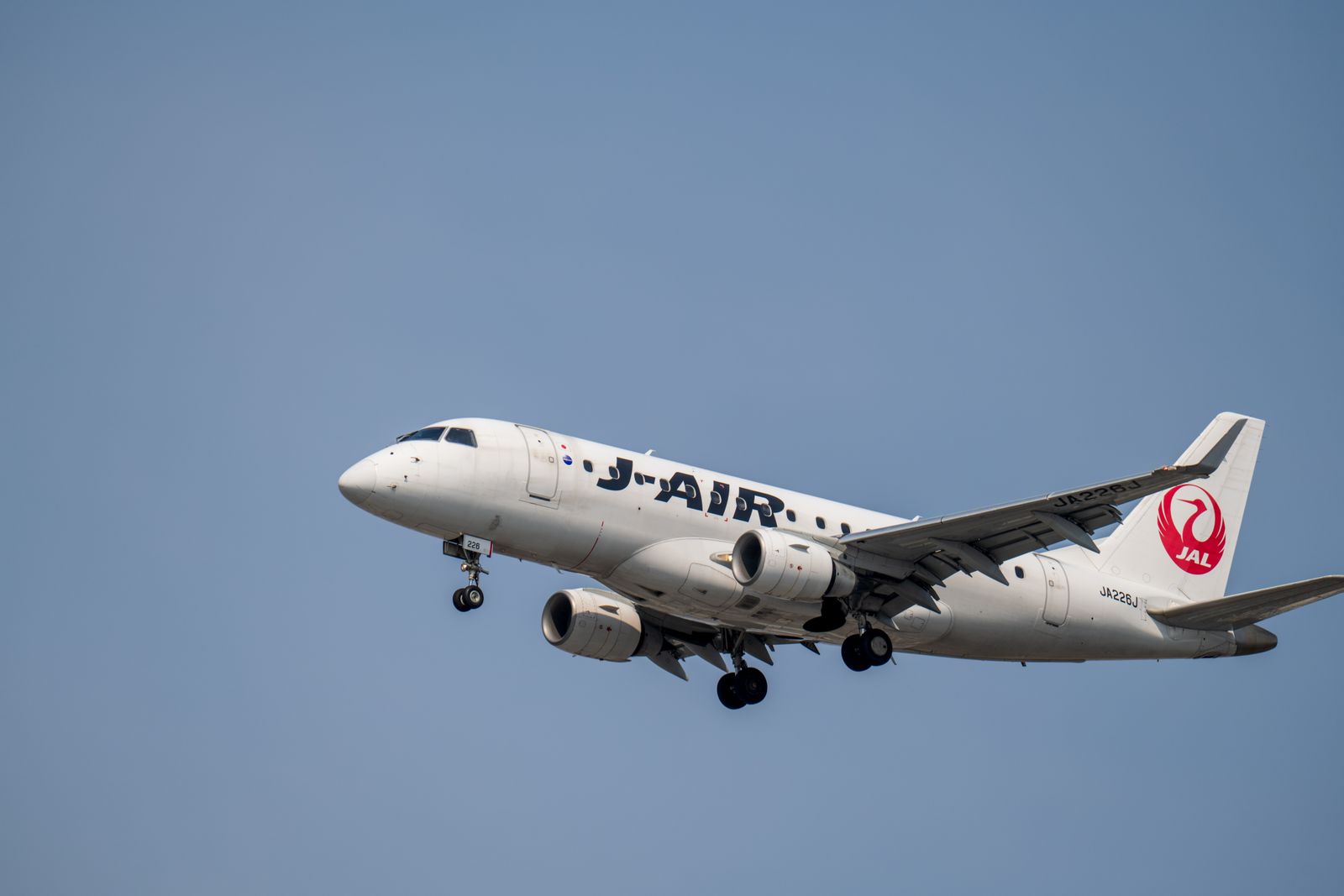 A J-Air regional jet in Japan Airlines colours climbing against a blue sky