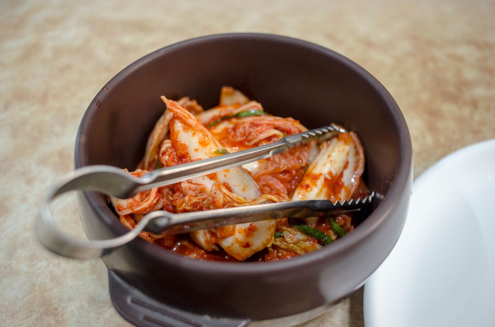 A bowl of napa cabbage kimchi with serving tongs