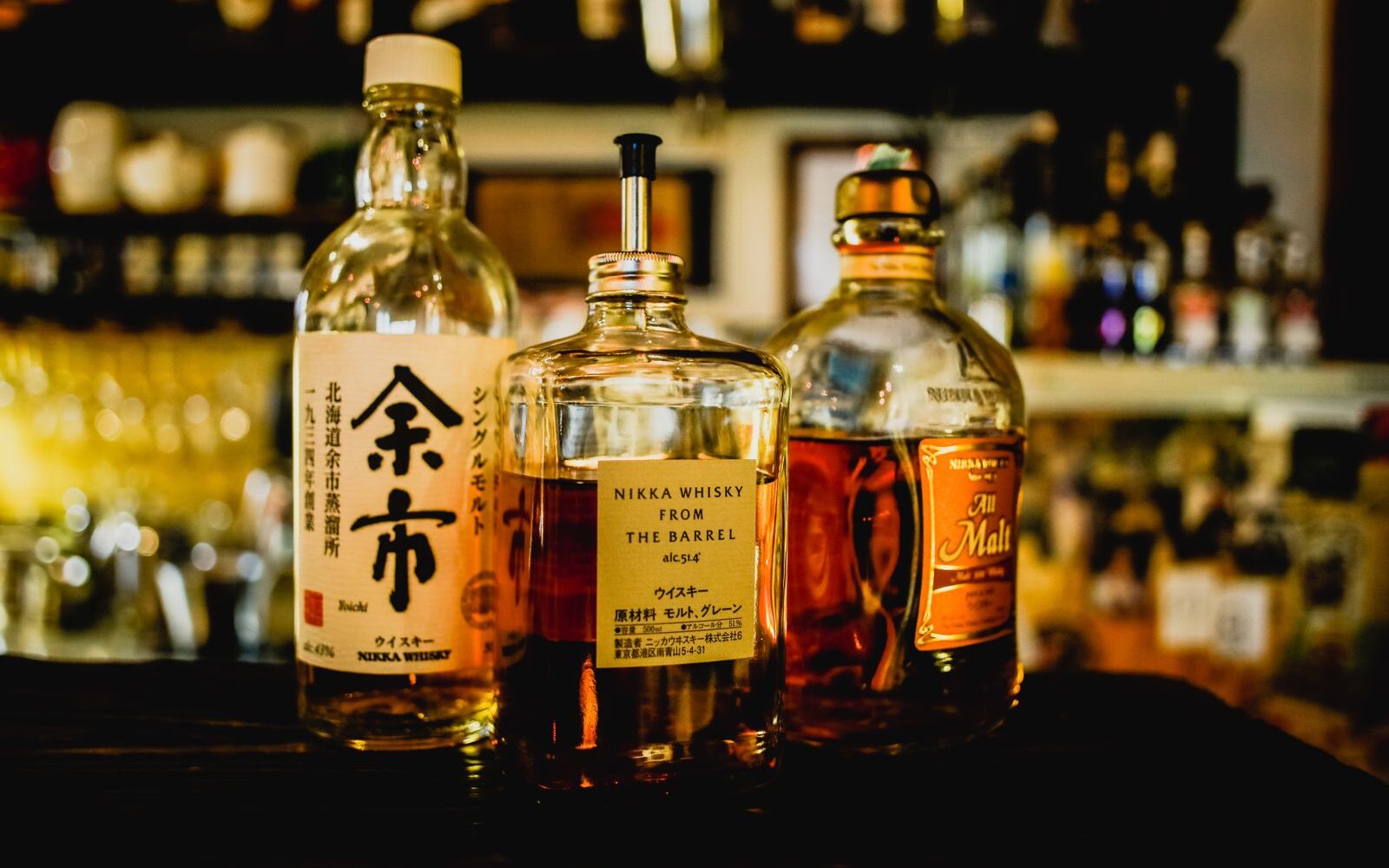 Bottles of Nikka Yoichi, Nikka From the Barrel and Nikka All Malt on a dimly lit bar counter
