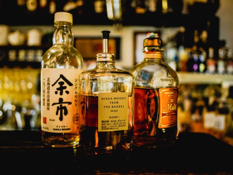 Bottles of Nikka Yoichi, Nikka From the Barrel and Nikka All Malt on a dimly lit bar counter