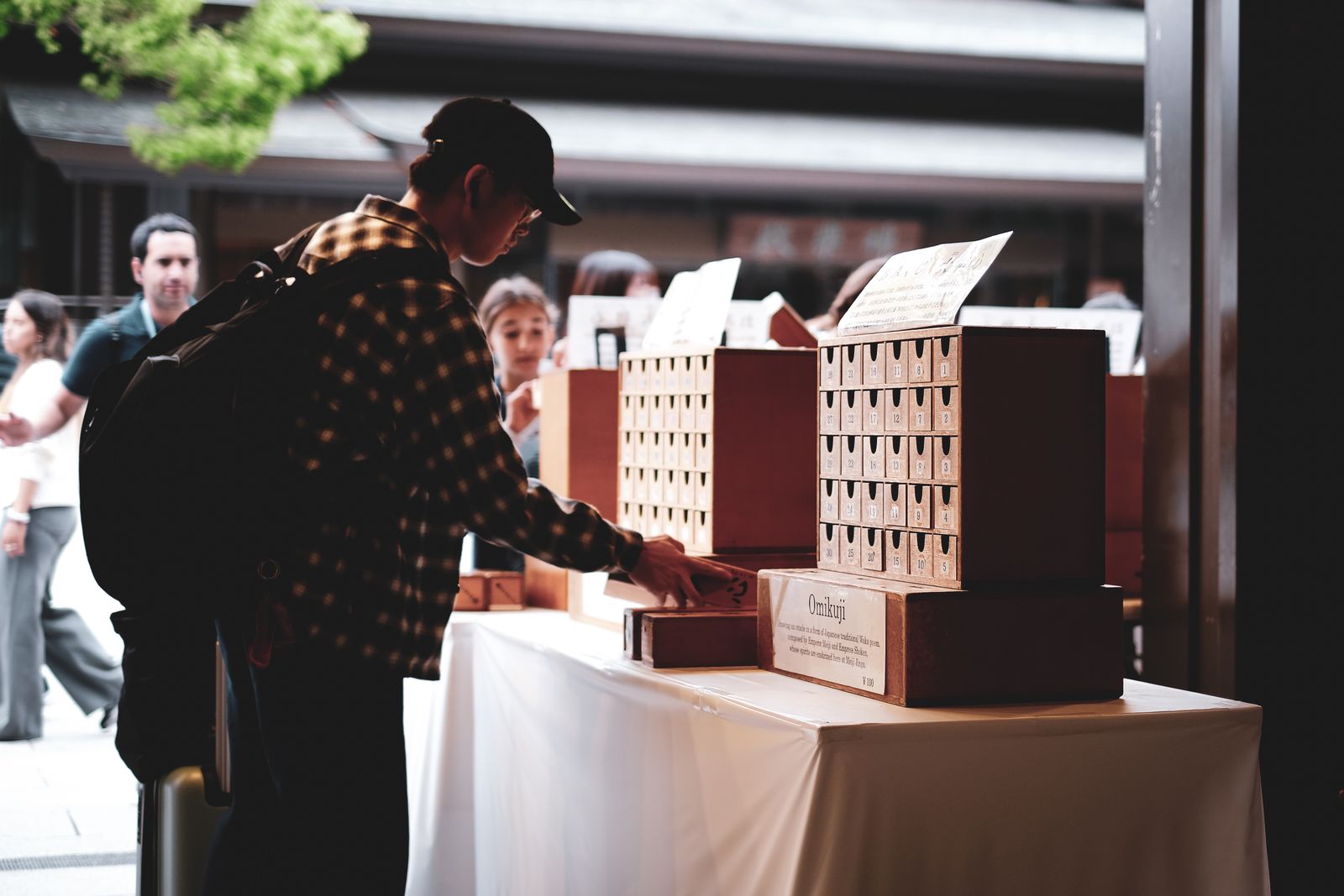 A visitor drawing an omikuji fortune from a wooden cabinet of numbered drawers at a shrine