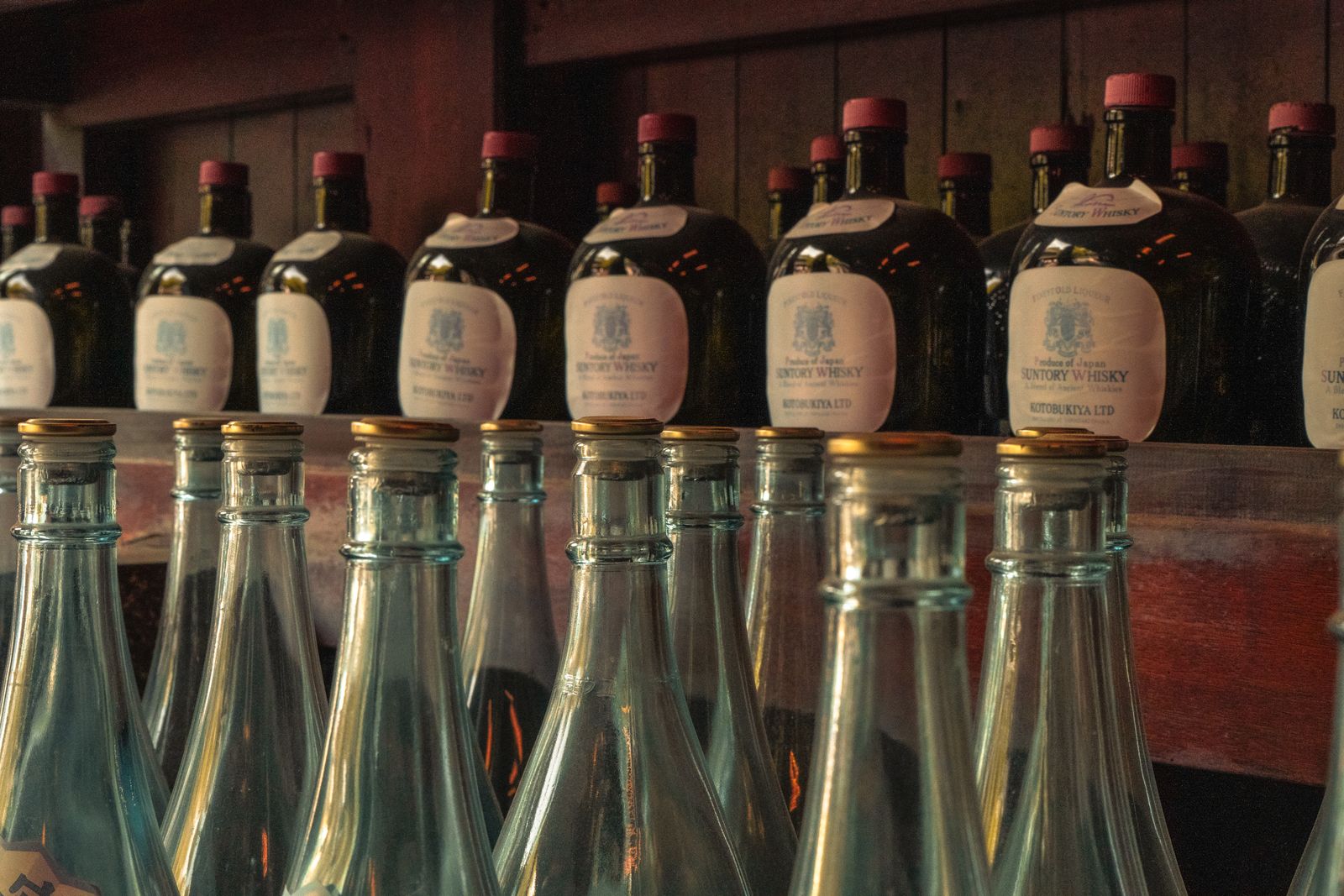 Old bottles of Suntory Whisky labelled Kotobukiya Ltd lined up on a wooden shelf above empty glass bottles