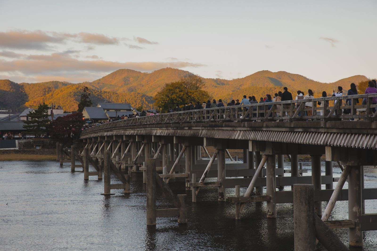 Crowds of visitors walking across the Togetsukyo Bridge at dusk