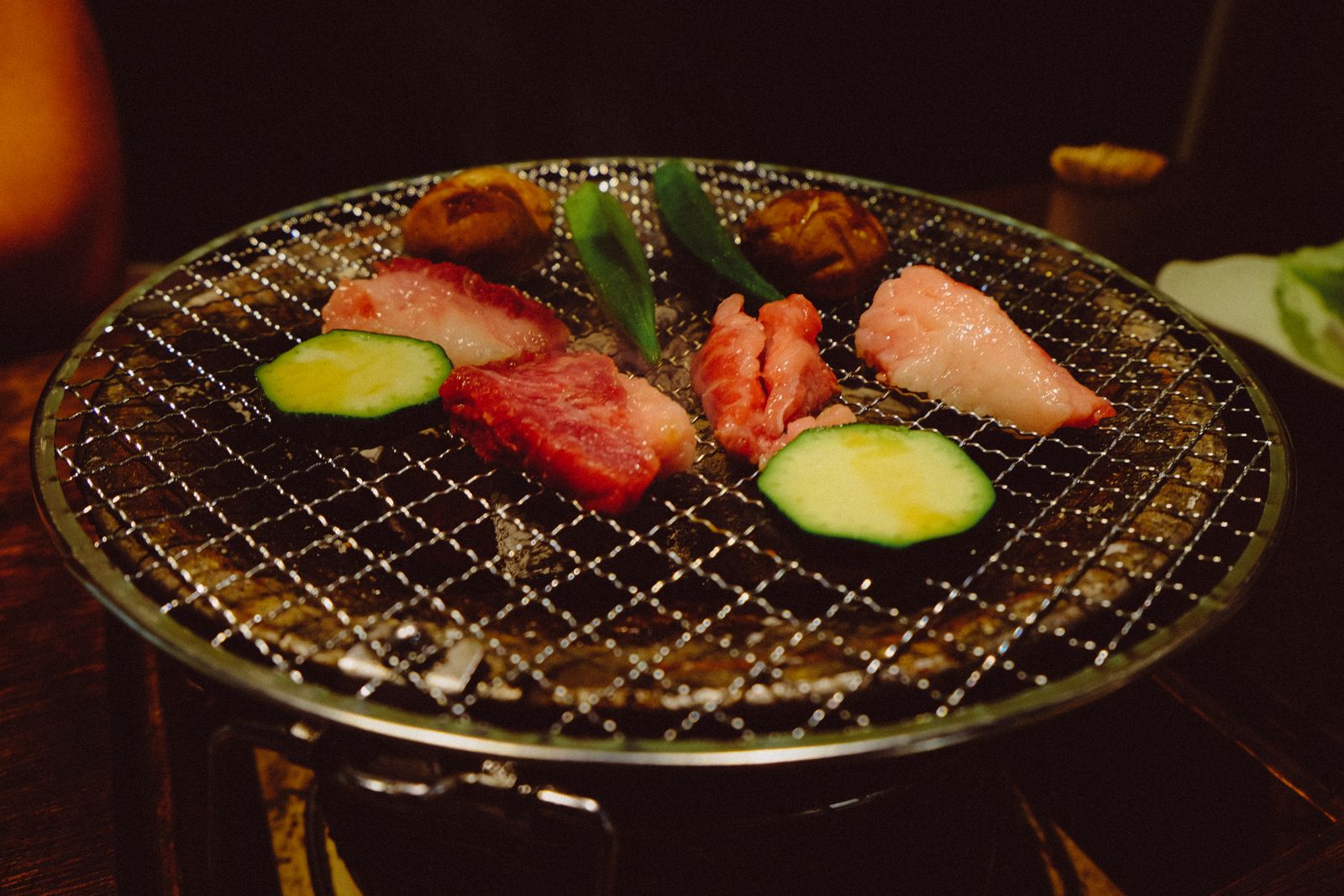 Beef, shiitake mushrooms and courgette grilling on a wire mesh over a small tabletop charcoal grill