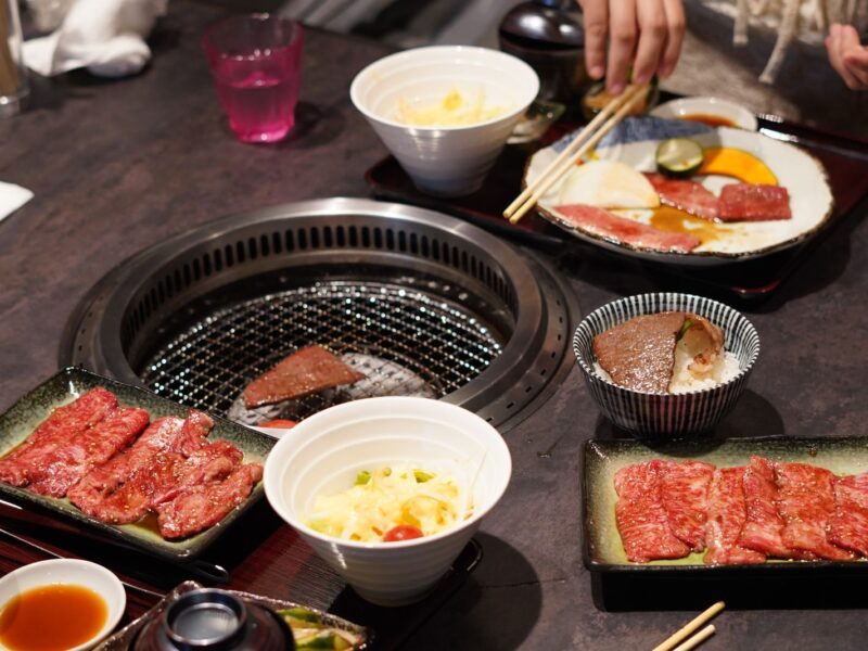 A yakiniku table with plates of marbled beef, rice bowls and salad set around a round built-in grill