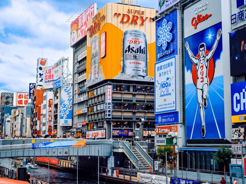 The Glico running man and Asahi signs above Ebisu Bridge on Dotonbori, Osaka, on a bright afternoon
