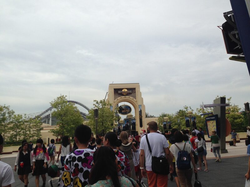 Adults and children walk toward the entrance arch at Universal Studios Japan in Osaka under an overcast sky.