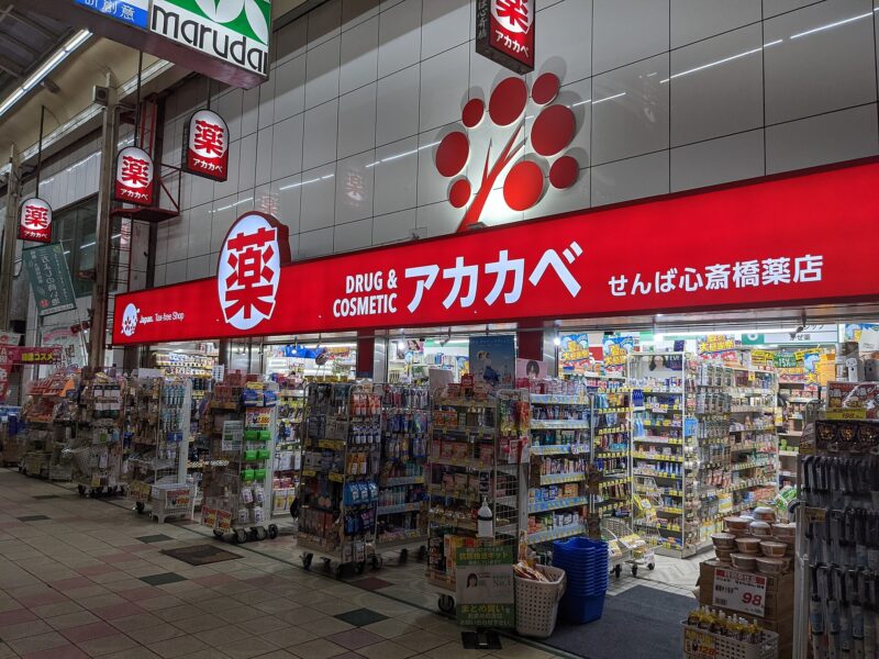 Akakabe in Osaka displays a Tax-free Shop sign above densely stocked drugstore shelves beneath a covered shopping arcade.