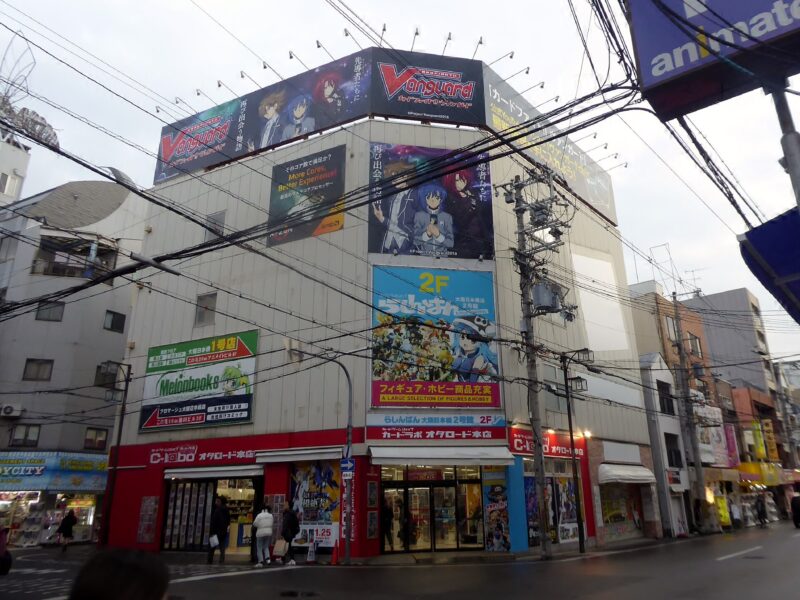 Anime billboards cover a corner building above card and figure shops on Otaku Road in Osaka’s Den Den Town.