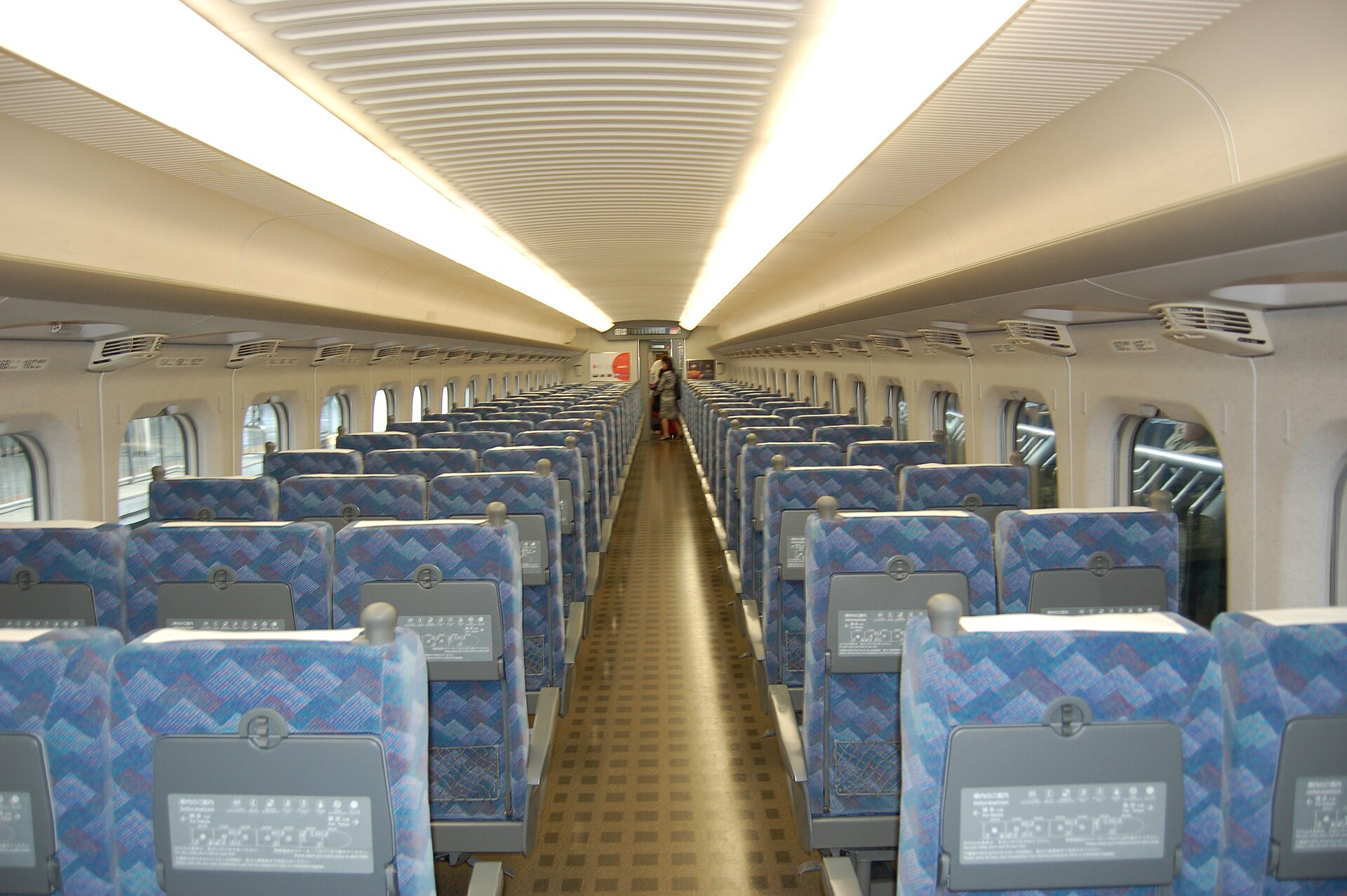 Blue patterned seats form rows of three and two around the central aisle inside an N700 Shinkansen carriage.