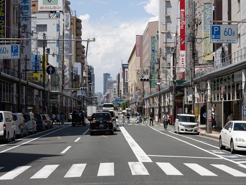 Cars and cyclists pass beneath vertical shop signs along the covered pavements of Den Den Town in Osaka.