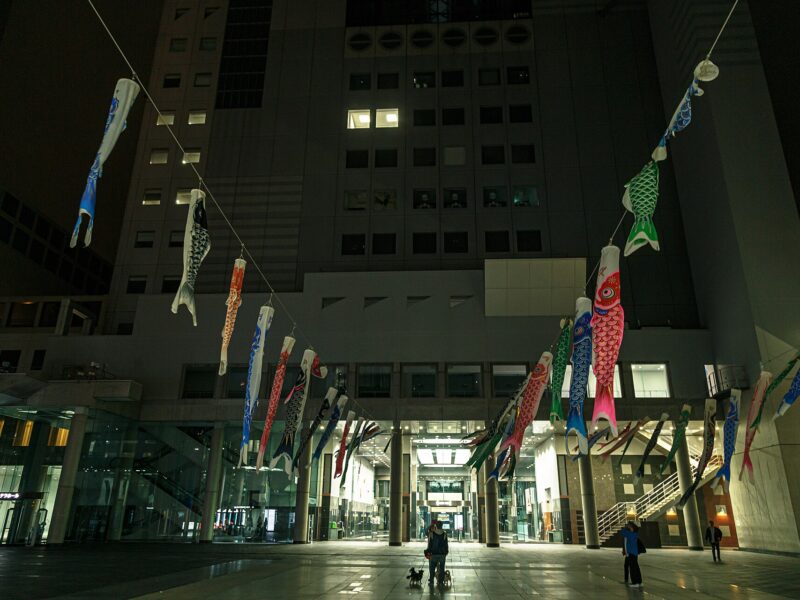 Colorful carp streamers hang above visitors in the plaza at Umeda Sky Building in Osaka at night.