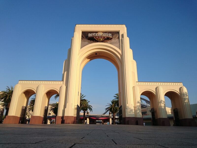 The cream entrance arch at Universal Studios Japan in Osaka stands above palm trees beneath a clear blue sky.