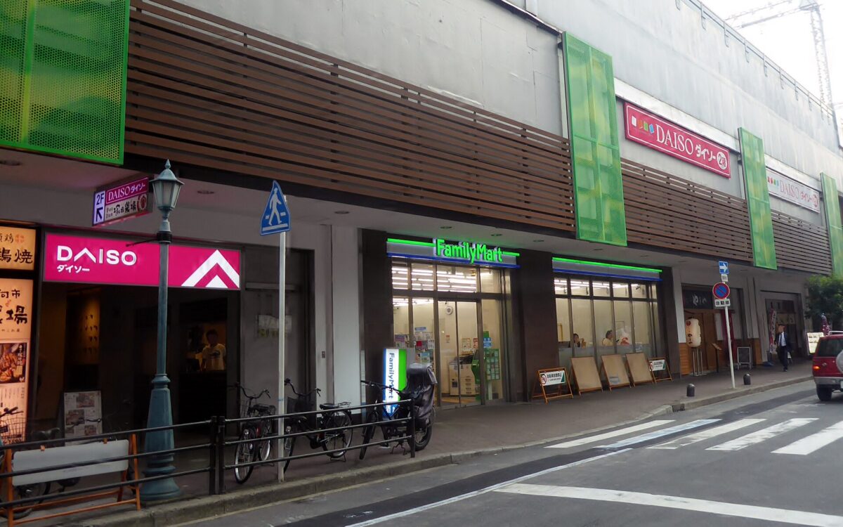 FamilyMart windows face a narrow street beside a Daiso entrance in the Kyobashi area of Osaka.