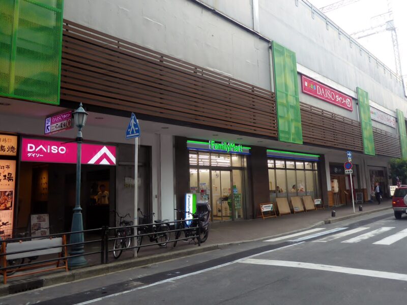 FamilyMart windows face a narrow street beside a Daiso entrance in the Kyobashi area of Osaka.