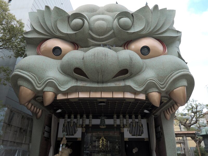 The giant green lion-head stage at Namba Yasaka Shrine in Osaka, with golden eyes and an open mouth.