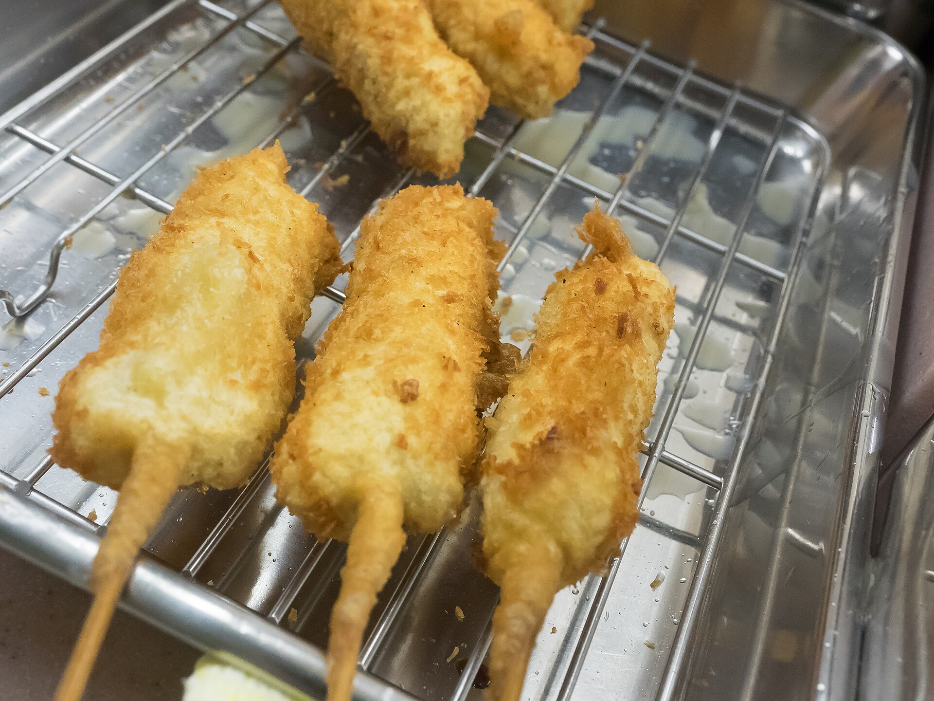 Golden kushikatsu skewers rest on a wire rack in a metal tray at Yaekatsu in Osaka, showing their crisp crumb coating.