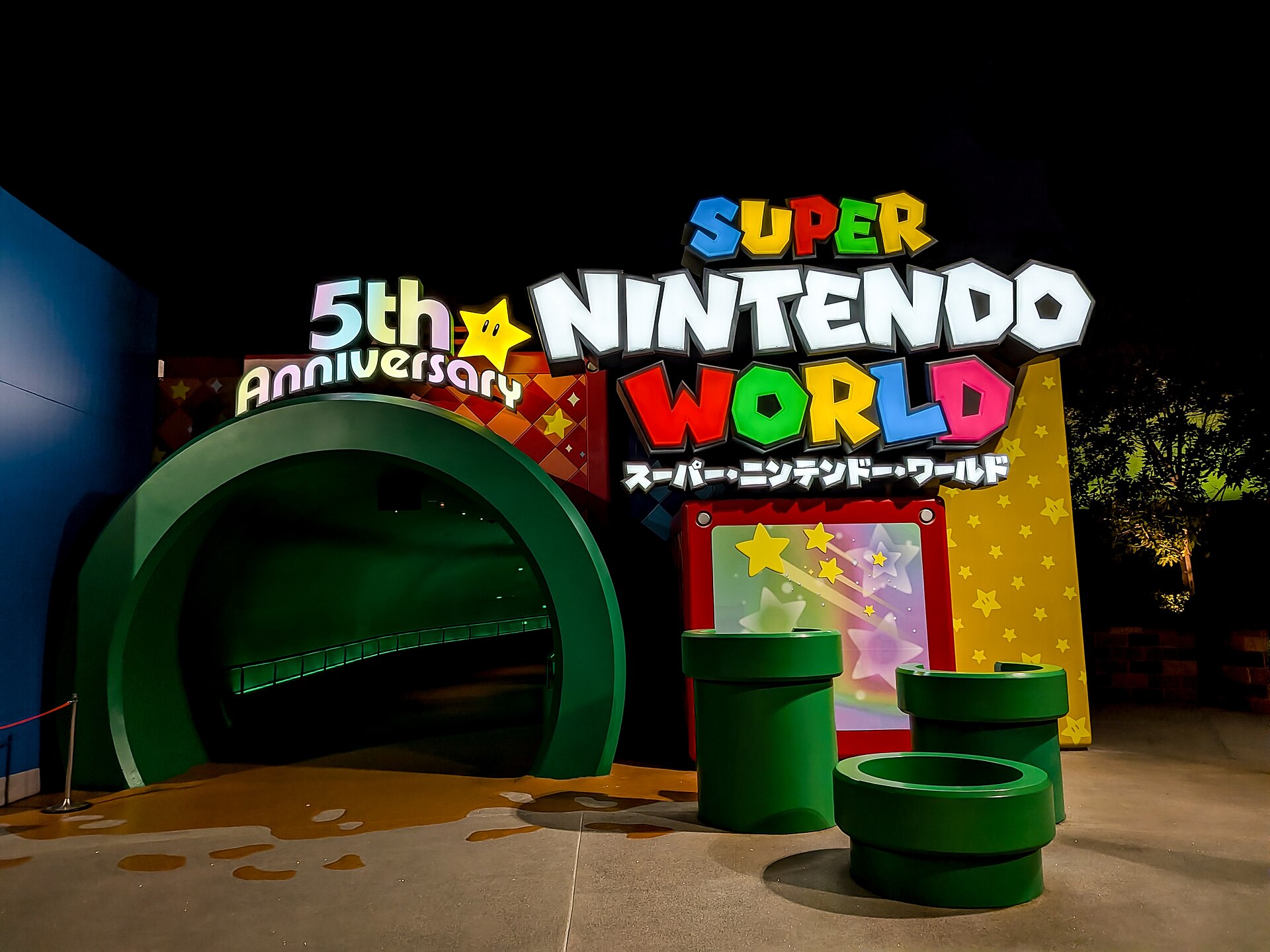 A green pipe tunnel and illuminated Super Nintendo World sign mark the entrance at Universal Studios Japan in Osaka at night.