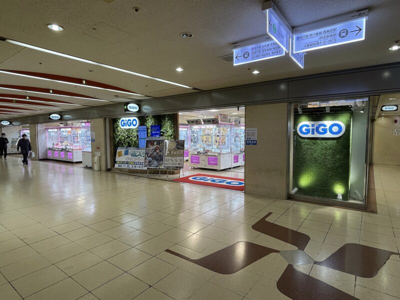 Illuminated crane-game cabinets fill the open entrance of GiGO in Osaka Ekimae Building No. 4 beside an underground concourse.