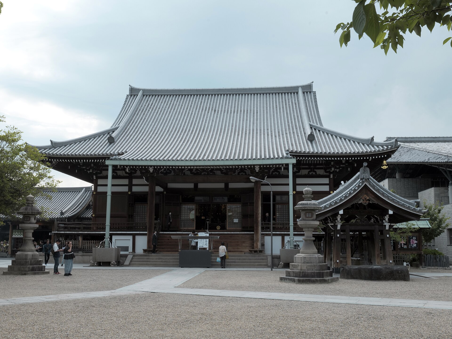 Isshinji’s main hall faces a gravel courtyard in Osaka, with a wide tiled roof, stone lanterns, and visitors beside the steps.