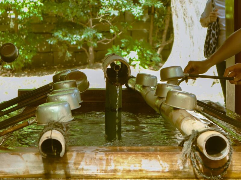 Visitors using bamboo-handled ladles to rinse their hands at a shrine water basin in Japan