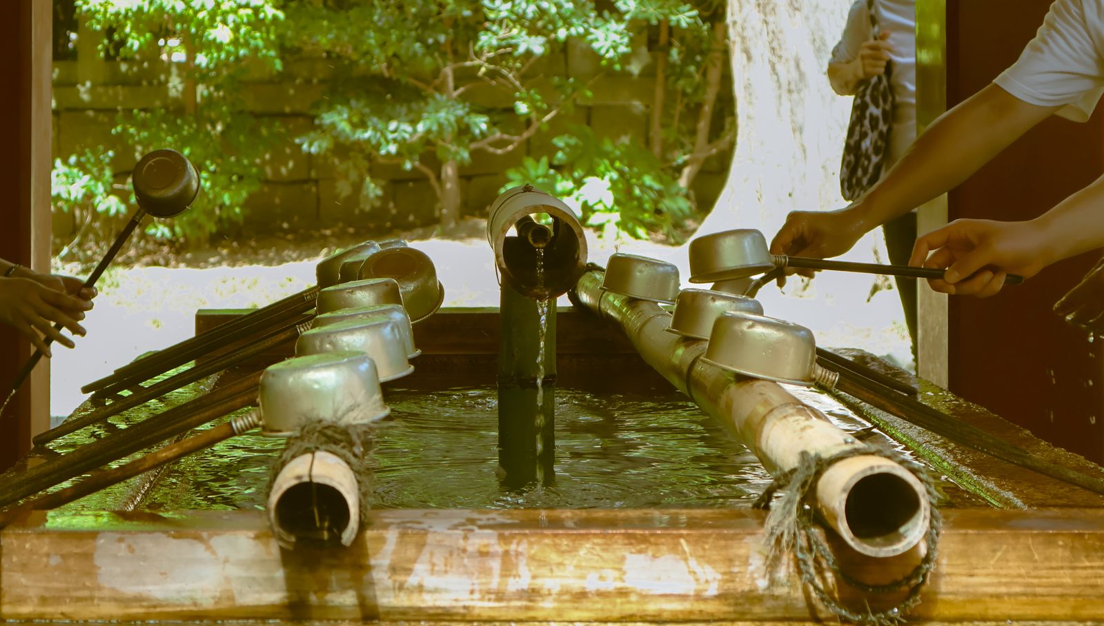 Visitors using bamboo-handled ladles to rinse their hands at a shrine water basin in Japan