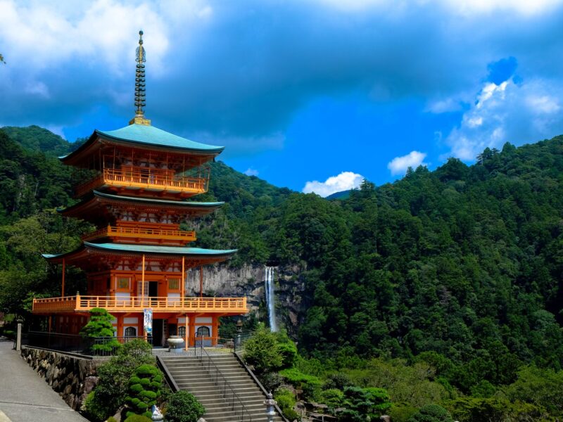The red three-storey pagoda of Seiganto-ji with Nachi Falls dropping down the forested mountainside behind it