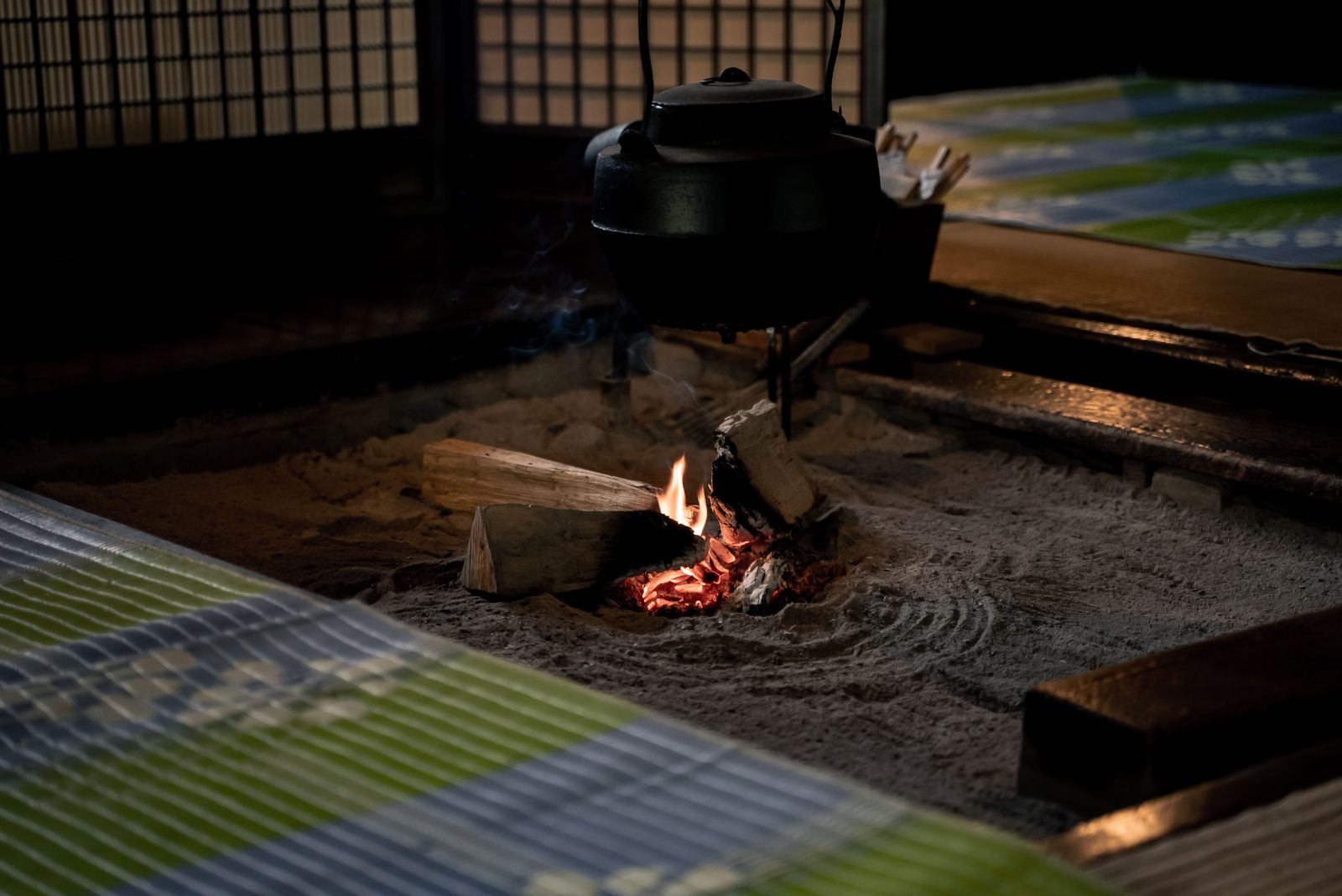 An iron kettle hanging over a small wood fire in a traditional sunken irori hearth