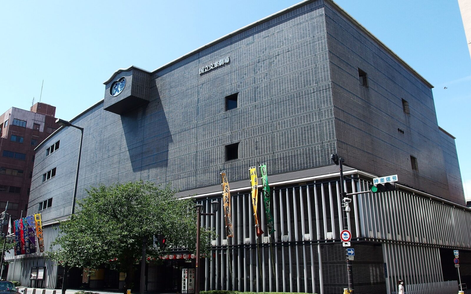 National Bunraku Theatre in Osaka with a projecting clock, grey facade and colourful banners beside the entrance.