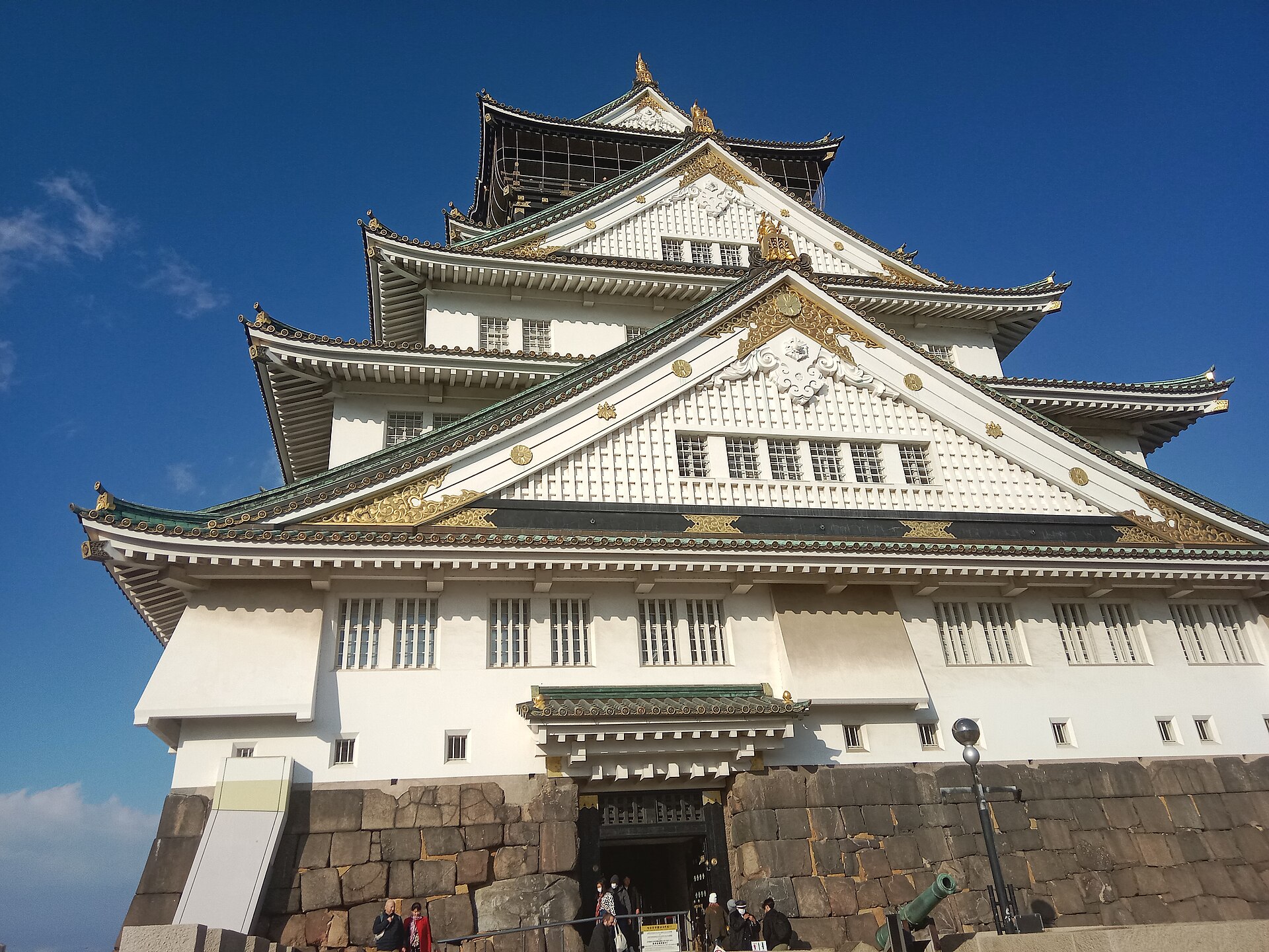 Osaka Castle's white keep and stone base stand beneath a blue January sky, with visitors at the entrance.