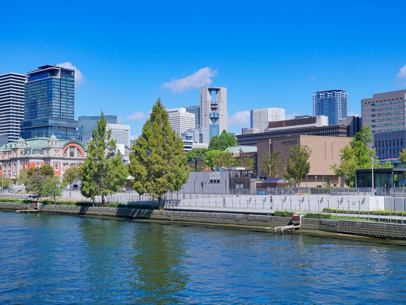 Osaka Central Public Hall and riverside museum buildings rise above the water on Nakanoshima under a blue sky.