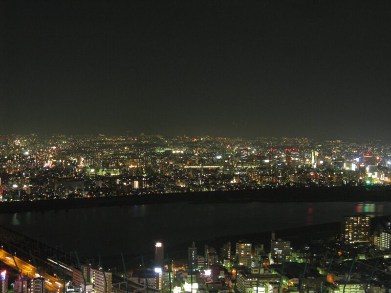 Osaka city lights spread beyond the dark Yodo River in a northward night view from Umeda Sky Building.