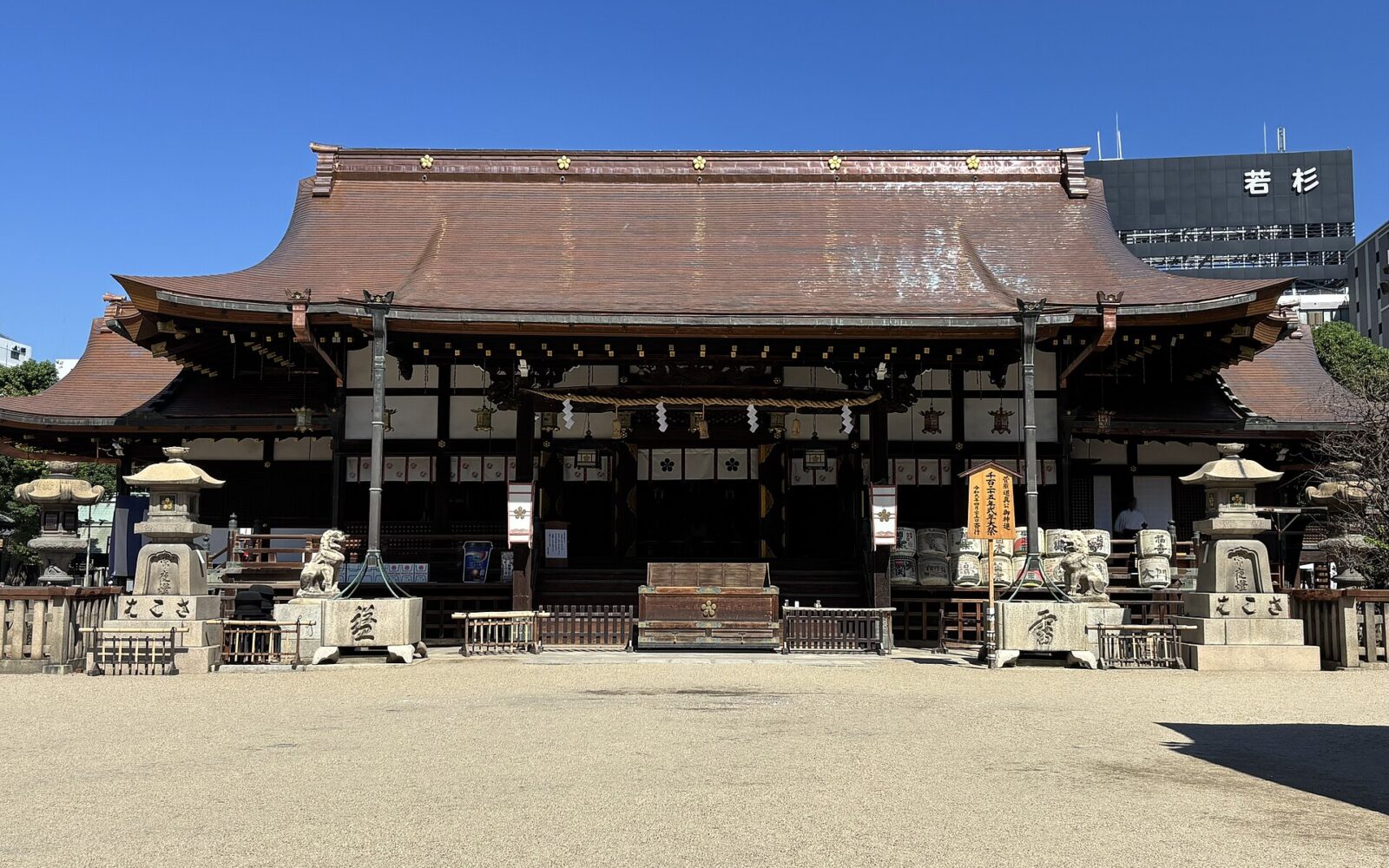 Osaka Tenmangu’s main hall faces a gravel courtyard beneath a broad copper-colored roof, flanked by stone lanterns and guardian animals.