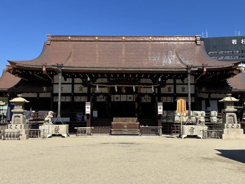 Osaka Tenmangu’s main hall faces a gravel courtyard beneath a broad copper-colored roof, flanked by stone lanterns and guardian animals.