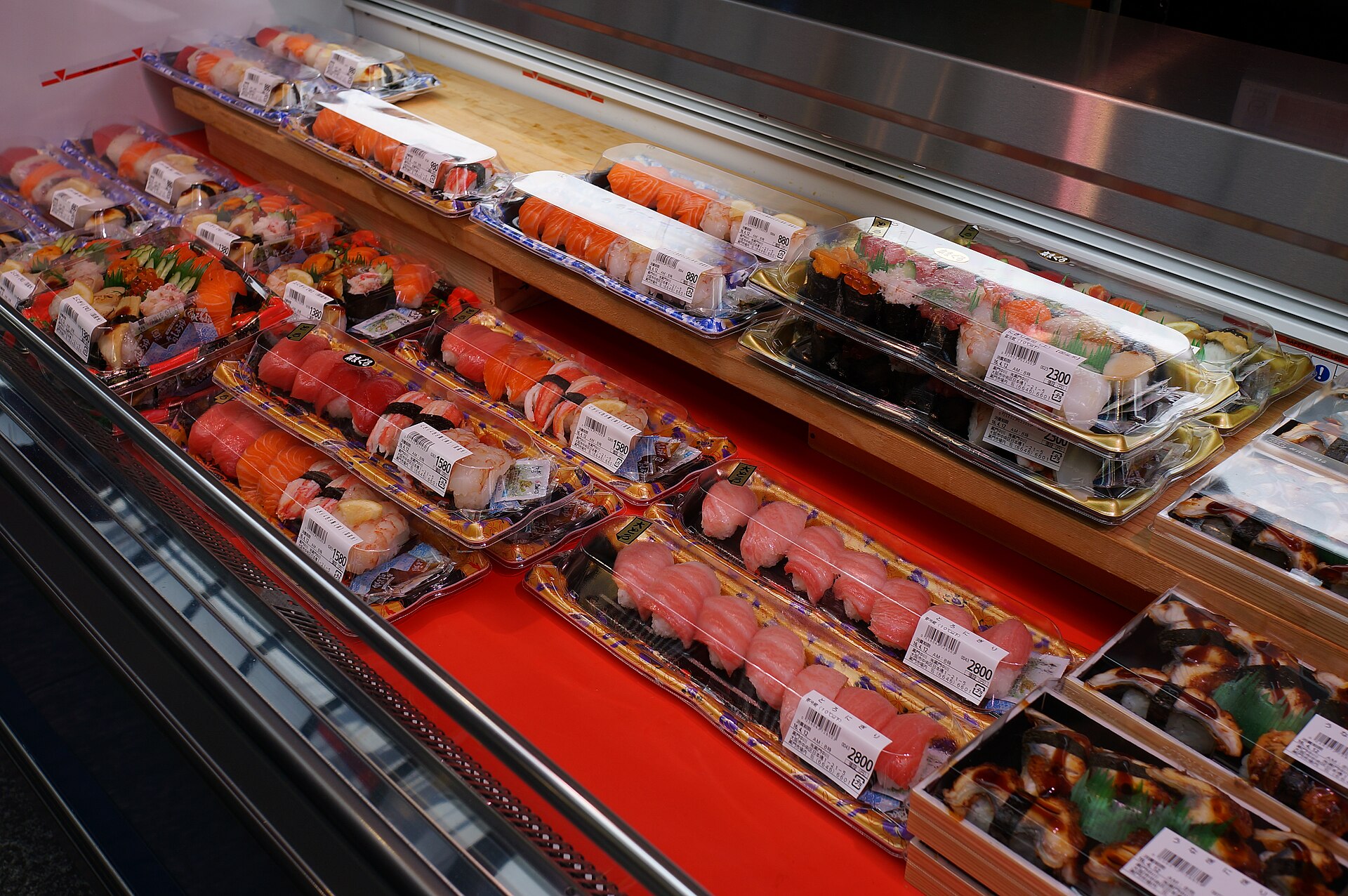 Packaged sushi with salmon, tuna and other toppings fills a red refrigerated display at Kuromon Market in Osaka.